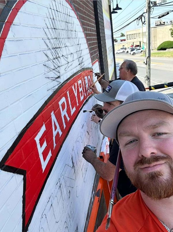 Three men painting a mural that says EARLYBIRD.