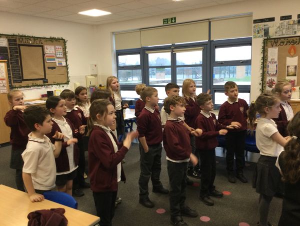 Group of schoolchildren standing and gesturing in a classroom.