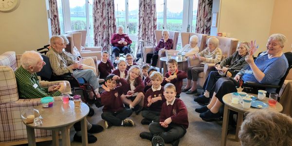 Children and elderly people gathered together in a cozy room, sharing smiles and peace signs.
