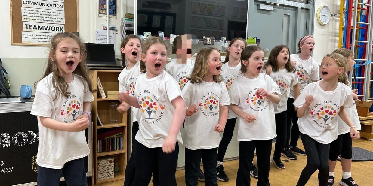 A group of children singing enthusiastically in matching choir t-shirts indoors.