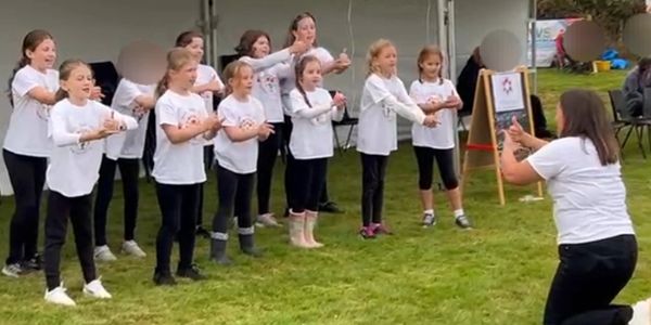 Group of girls in white shirts performing a synchronized dance outdoors.