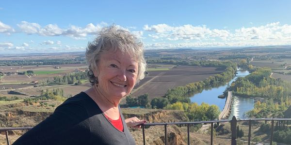 Smiling elderly woman overlooking a scenic river and farmland landscape.