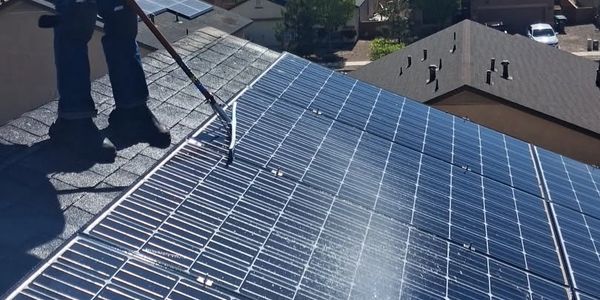 Person cleaning solar panels on a roof using a long-handled brush.