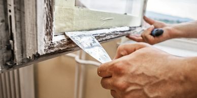 Person scraping old paint off a wooden window frame with a putty knife.