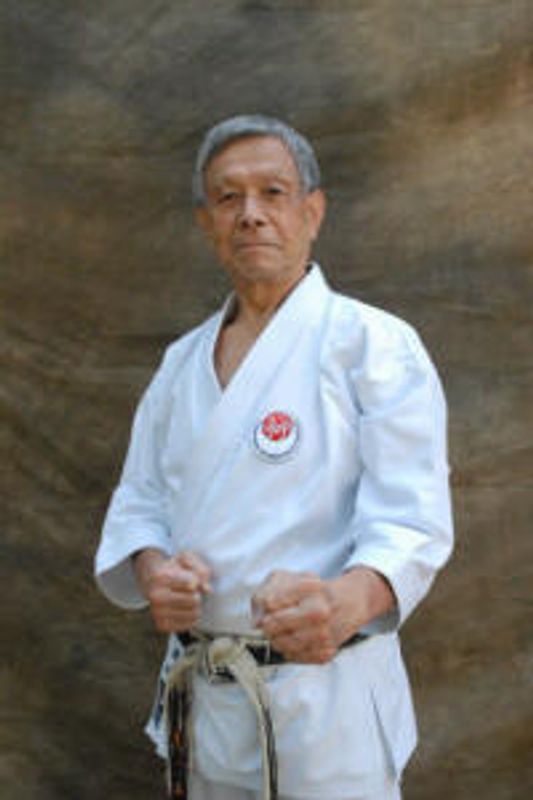 Elderly martial artist in white gi with black belt.