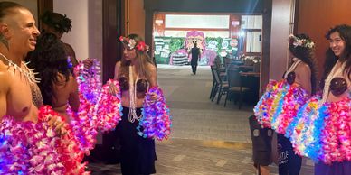 People dressed in colorful Hawaiian attire holding leis indoors.