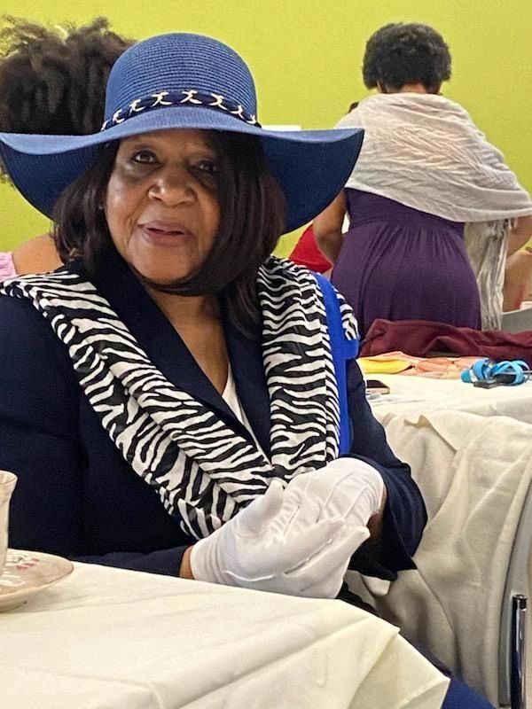 Elegant woman in a blue hat and zebra-patterned scarf sitting at a table.