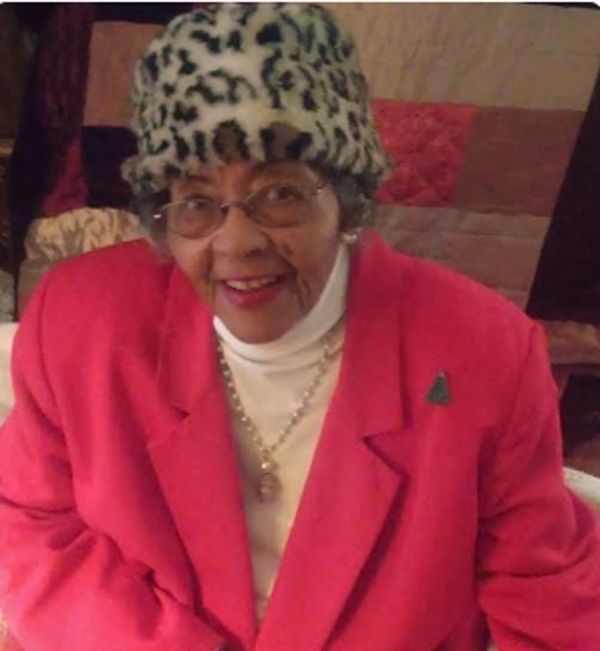 Elderly woman wearing leopard print hat and red coat smiling warmly.