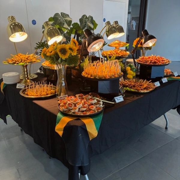 Catering table with various appetizers and sunflowers under warm lights.