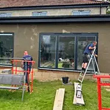 Two workers installing or repairing windows on a building exterior.