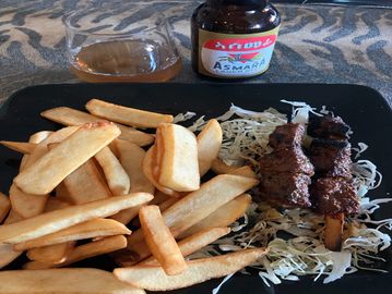 Plate with thick-cut fries and two grilled meat skewers on shredded cabbage.
