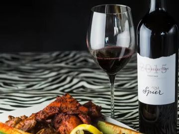 Glass of red wine with a bottle and grilled meat on a zebra print table.