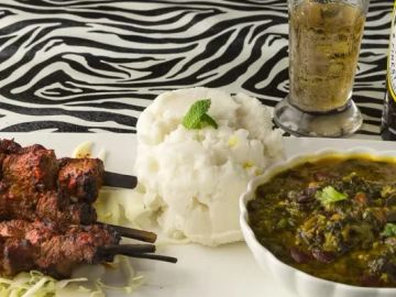 Grilled meat skewers with mashed potatoes and green vegetable curry on a zebra-striped tablecloth.