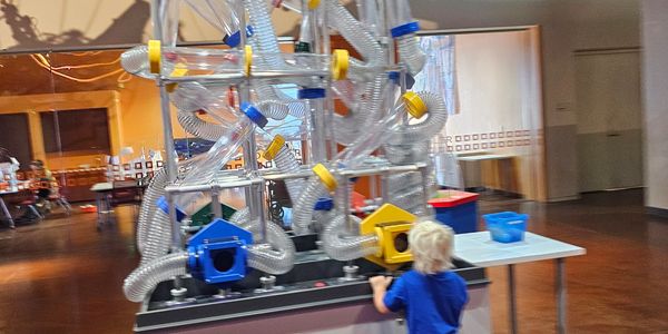 Child interacting with a large, complex tube exhibit in a museum.