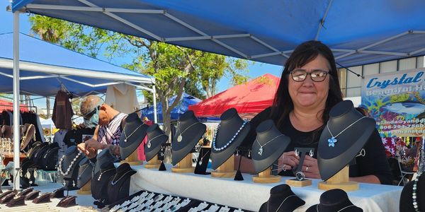 Woman selling handmade jewelry at an outdoor market stall.