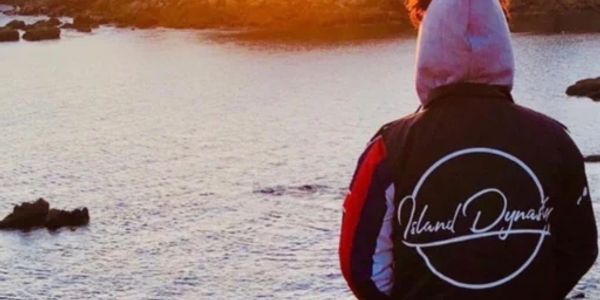 Person in a hoodie and jacket by the water at sunset.