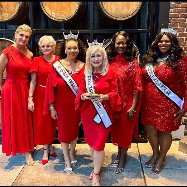 Group of six women in red dresses posing with crowns and sashes.