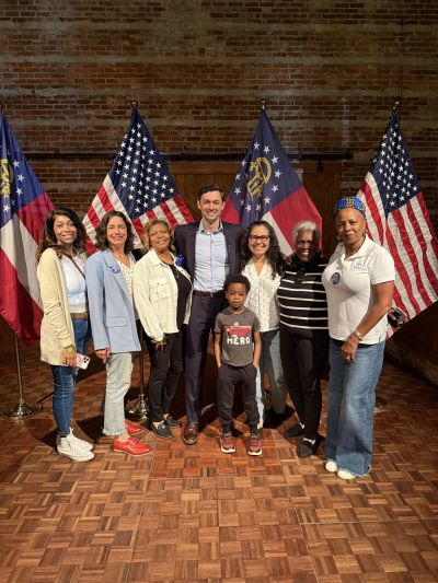 Group of diverse people posing in front of American and Georgia flags indoors.