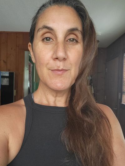 Woman with long brown hair wearing a black tank top indoors.