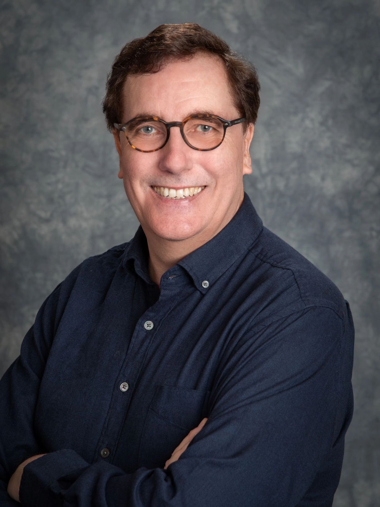 Smiling man with glasses and navy shirt.