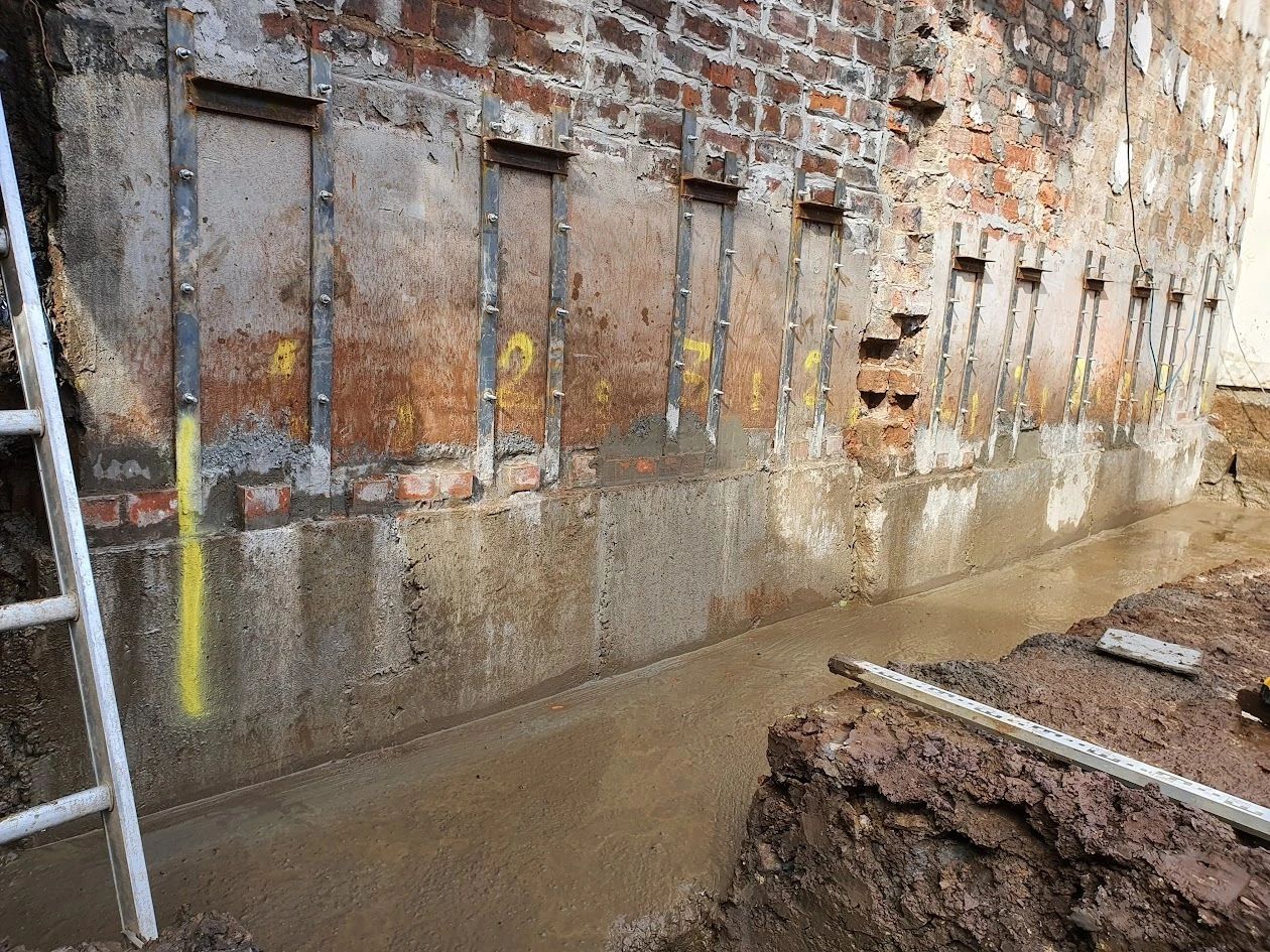 Reinforced brick wall with wet concrete base and construction tools nearby.