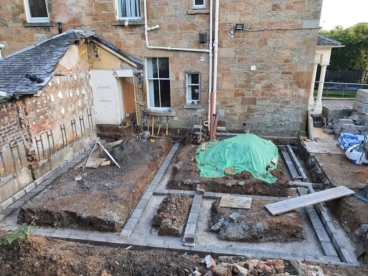 Construction site with foundation work in progress next to a brick house.