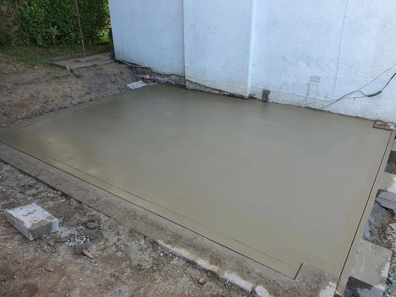 Freshly poured and smoothed concrete slab next to a white building.