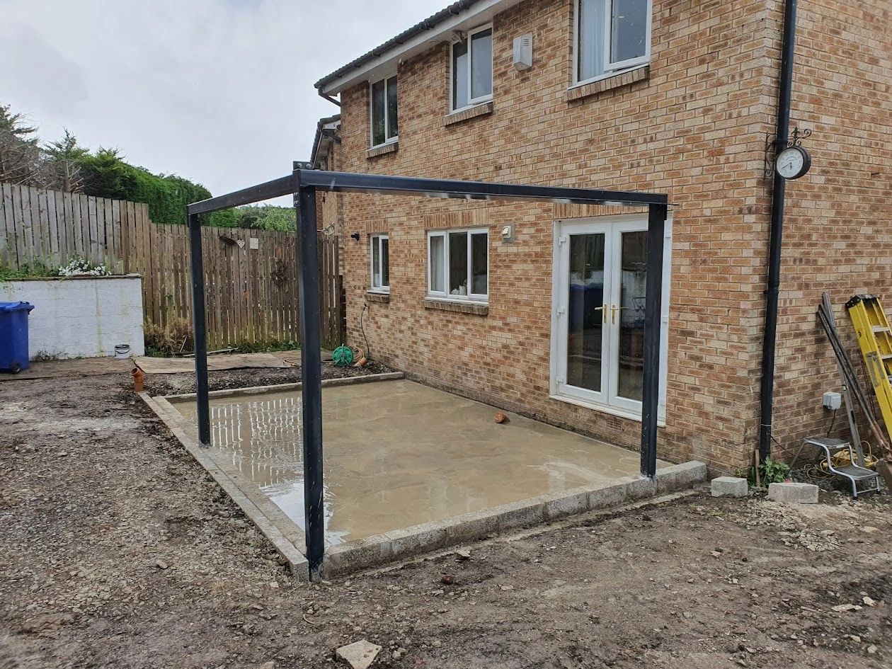A partially constructed patio area with metal frame outside a brick house.