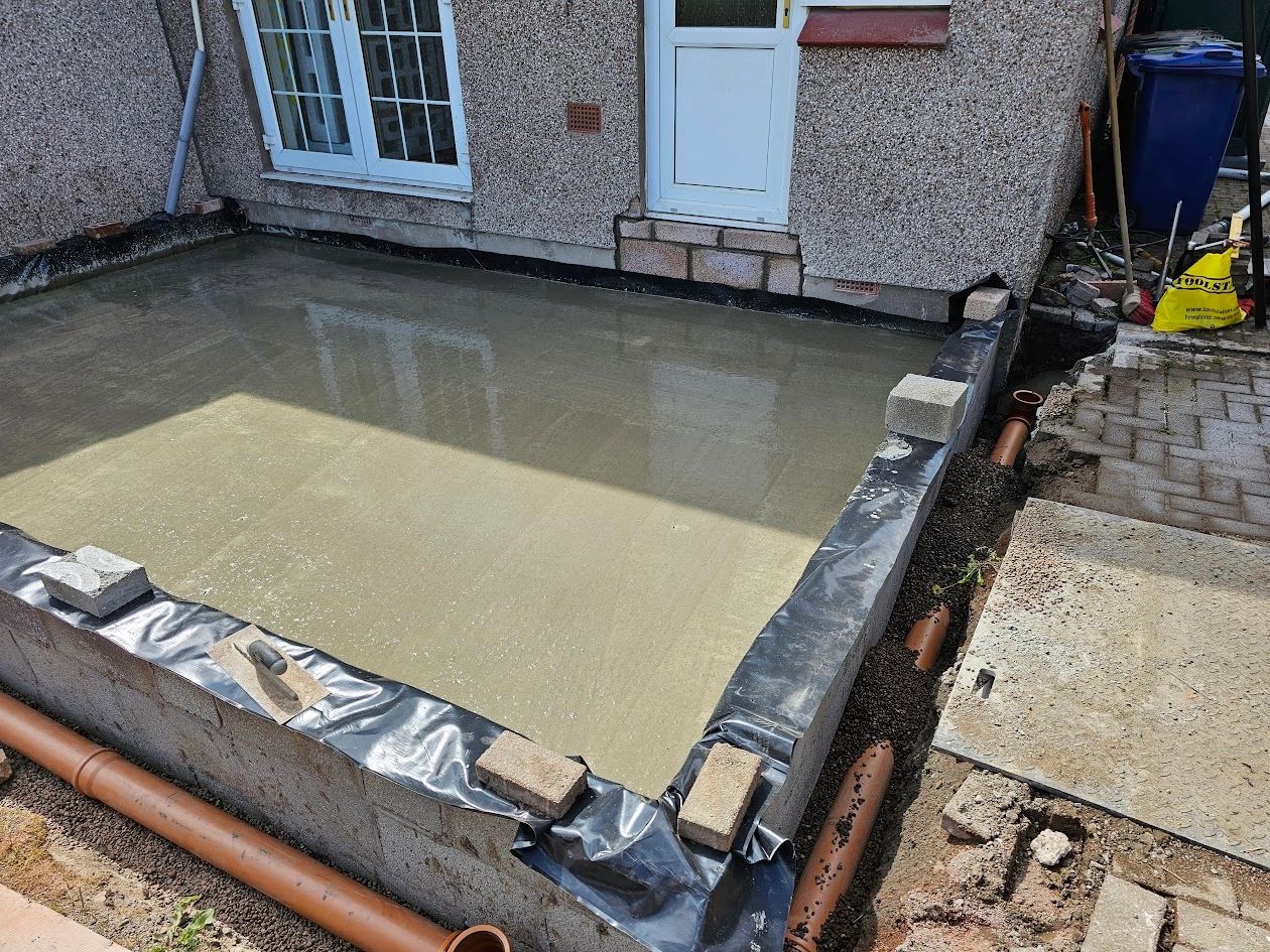 Fresh concrete slab foundation being laid outside a house.
