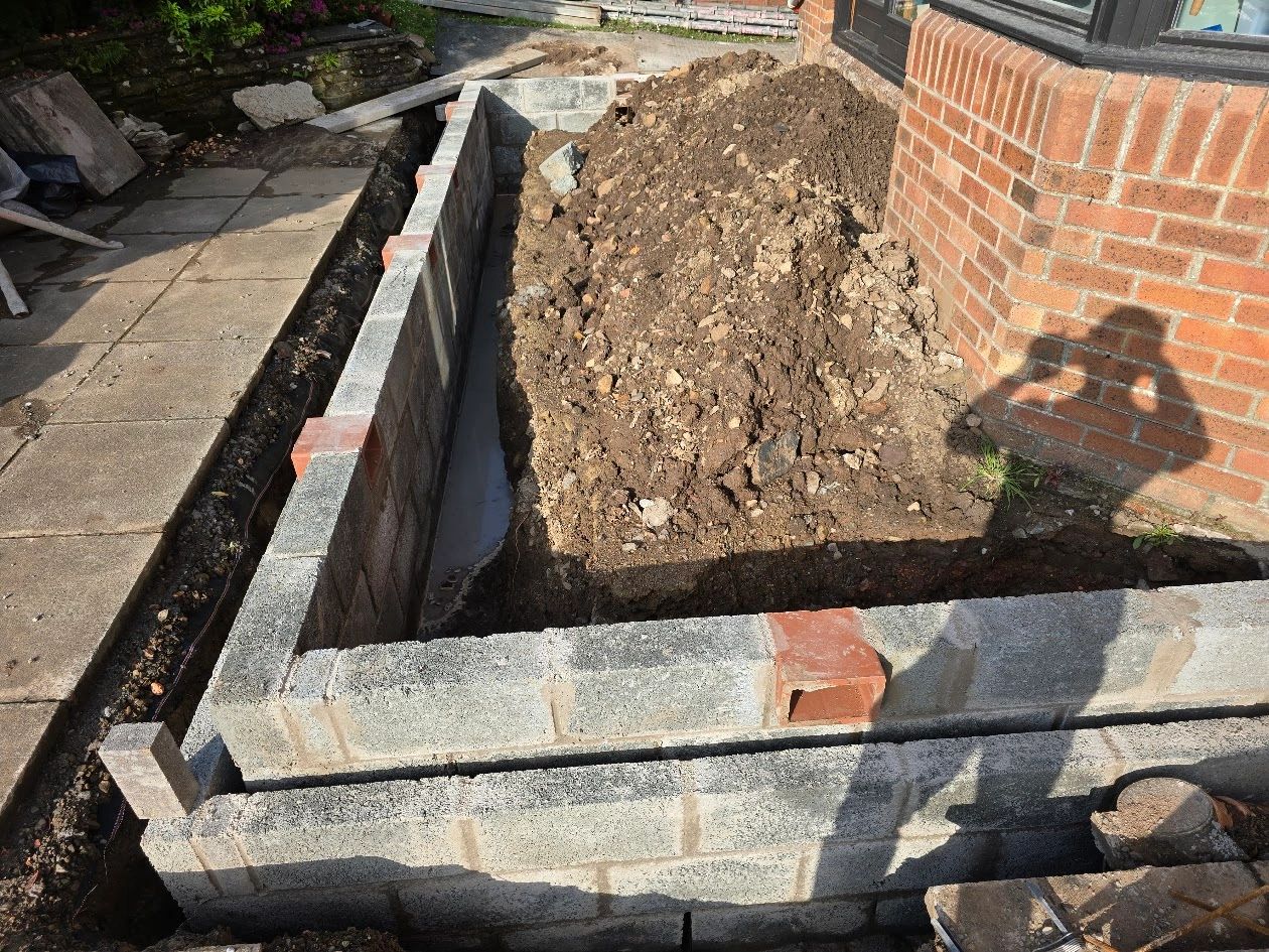 Construction site with a partially built brick wall and a pile of dirt.