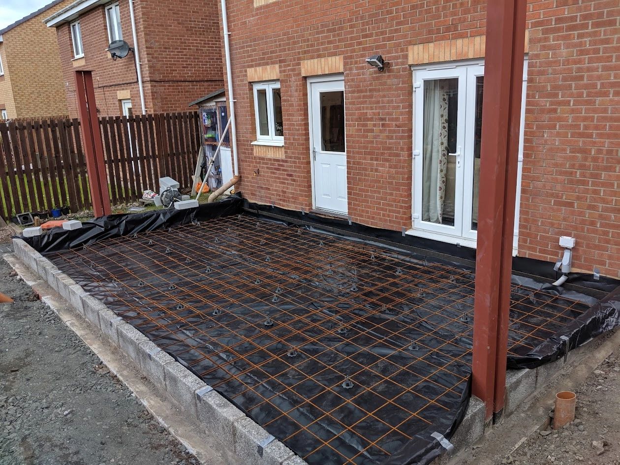 Construction site with steel reinforcement grid and plastic sheet foundation.