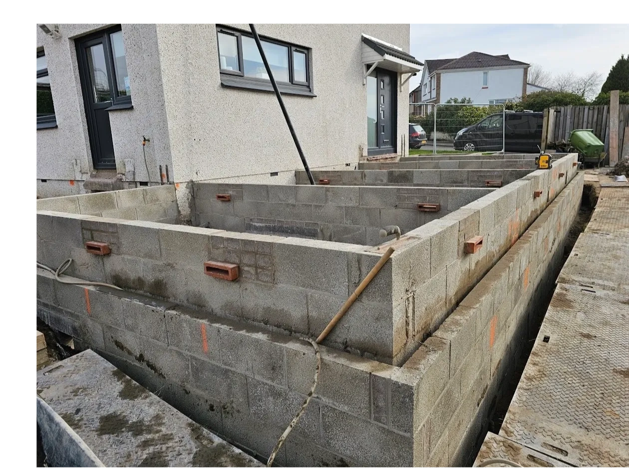 Concrete block foundation walls under construction beside a house.