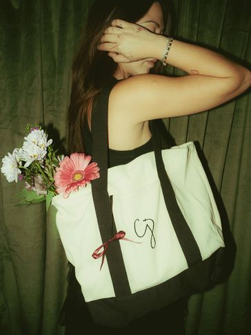 Woman holding a tote bag with flowers, partially covering her face.