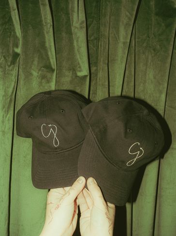 Two black caps with white lettering held against a green velvet curtain.