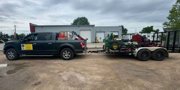 Black pickup truck towing a trailer with lawn equipment.