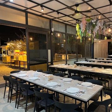 Elegant outdoor dining area with long tables set for guests under ceiling lights.