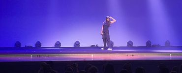 A performer stands alone on a lit stage with purple lighting.