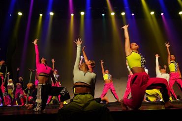A vibrant group dance performance with colorful lights and dynamic poses on stage.