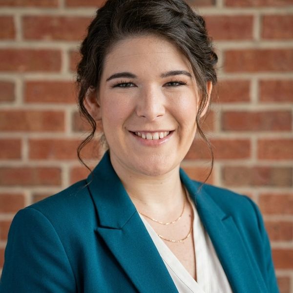 Professional woman smiling in teal blazer against a brick wall.