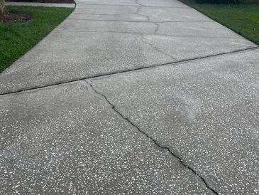 Concrete driveway with visible cracks and grass on sides.
