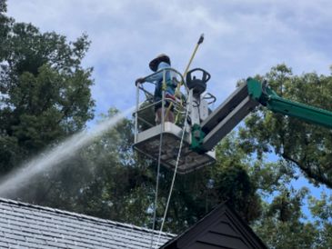 Worker on a lift power washing a roof on a sunny day.
