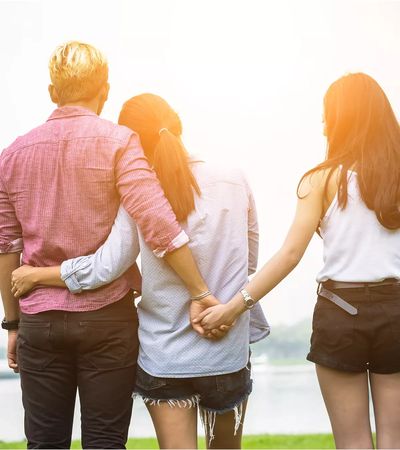 three people standing with two people embraced and one holding hands with one person in a a throuple