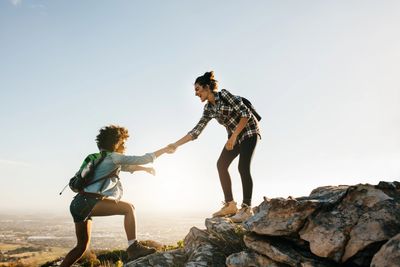 image of two women climbing a mountain side, with one helping the other step up by the hand