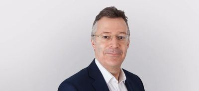 Middle-aged man in a suit with glasses against a plain background.