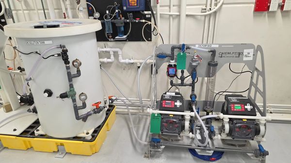 Industrial chemical dosing system with solution tank and pumps on a yellow spill containment pallet.