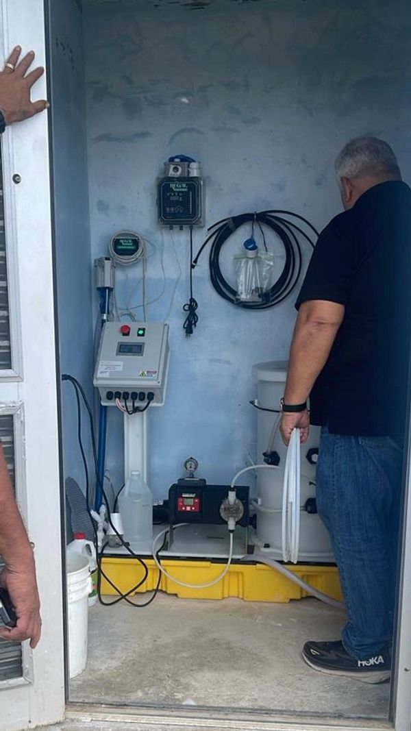 Two men inspecting water treatment equipment inside a small room.