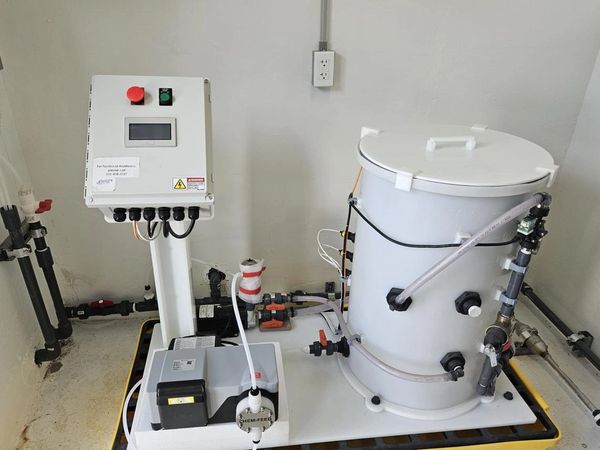 Chemical dosing system with control panel and containment platform in a utility room.