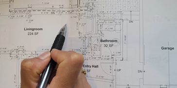 Hand holding a pen over a house floor plan with labeled rooms.
