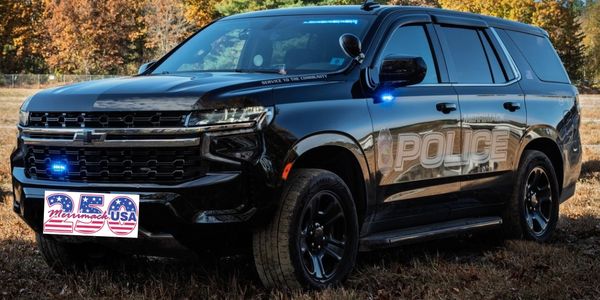 Black police SUV with blue lights on, parked outdoors.
