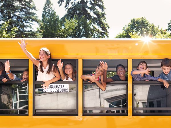 Excited children waving out the windows of a yellow school bus